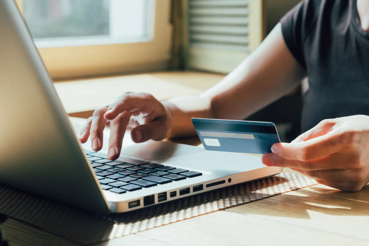 A person uses a laptop while holding a credit card, suggesting online shopping or electronic payment.