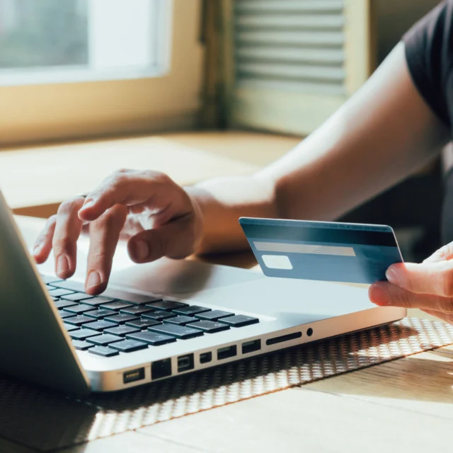 A person uses a laptop while holding a credit card, suggesting online shopping or electronic payment.