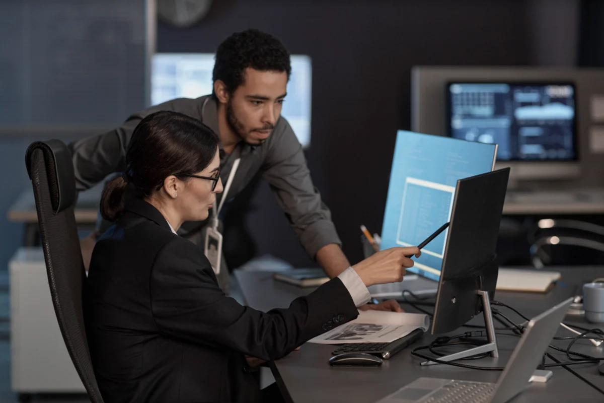 Two people pointing at computer screen while working in IT company.