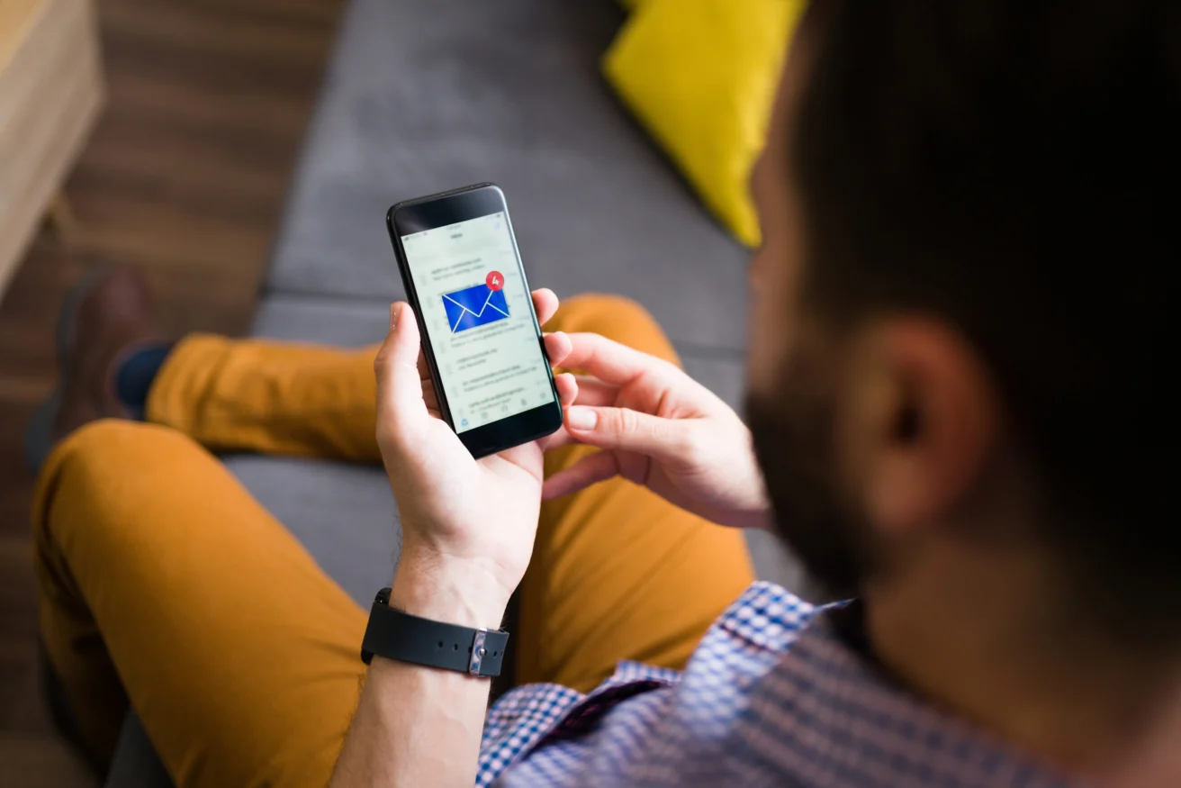 Adult man receiving a notification on his smartphone for a new e-mail while relaxing on the sofa