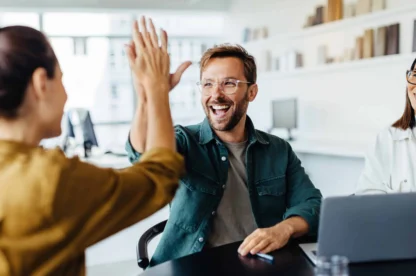 Successful business people giving each other a high five in a meeting. Two young business professionals celebrating teamwork in an office.