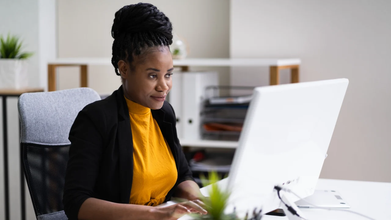 Professional woman working at a desktop computer in a modern office, focused on reviewing content on her screen